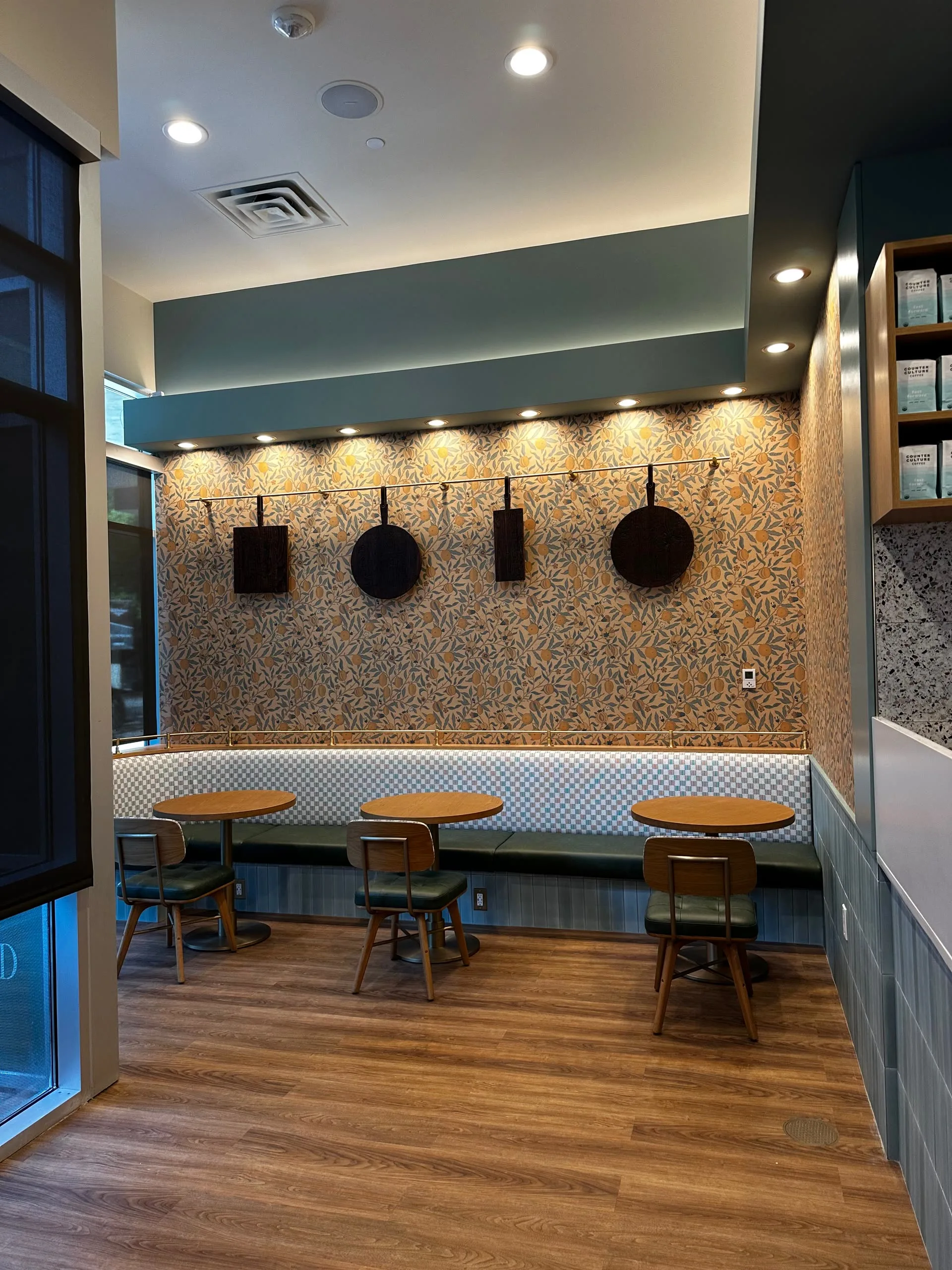 Banquette seating with small round tables beneath a speckled feature wall and hanging decorative panels