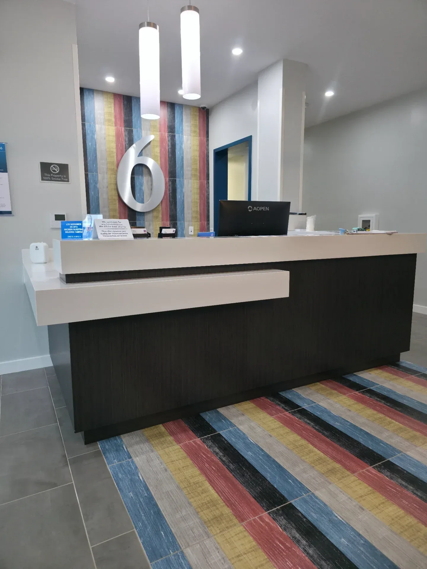 Dark wood-laminate U-shaped check-in desk with white quartz top in a hotel lobby with striped accent wall