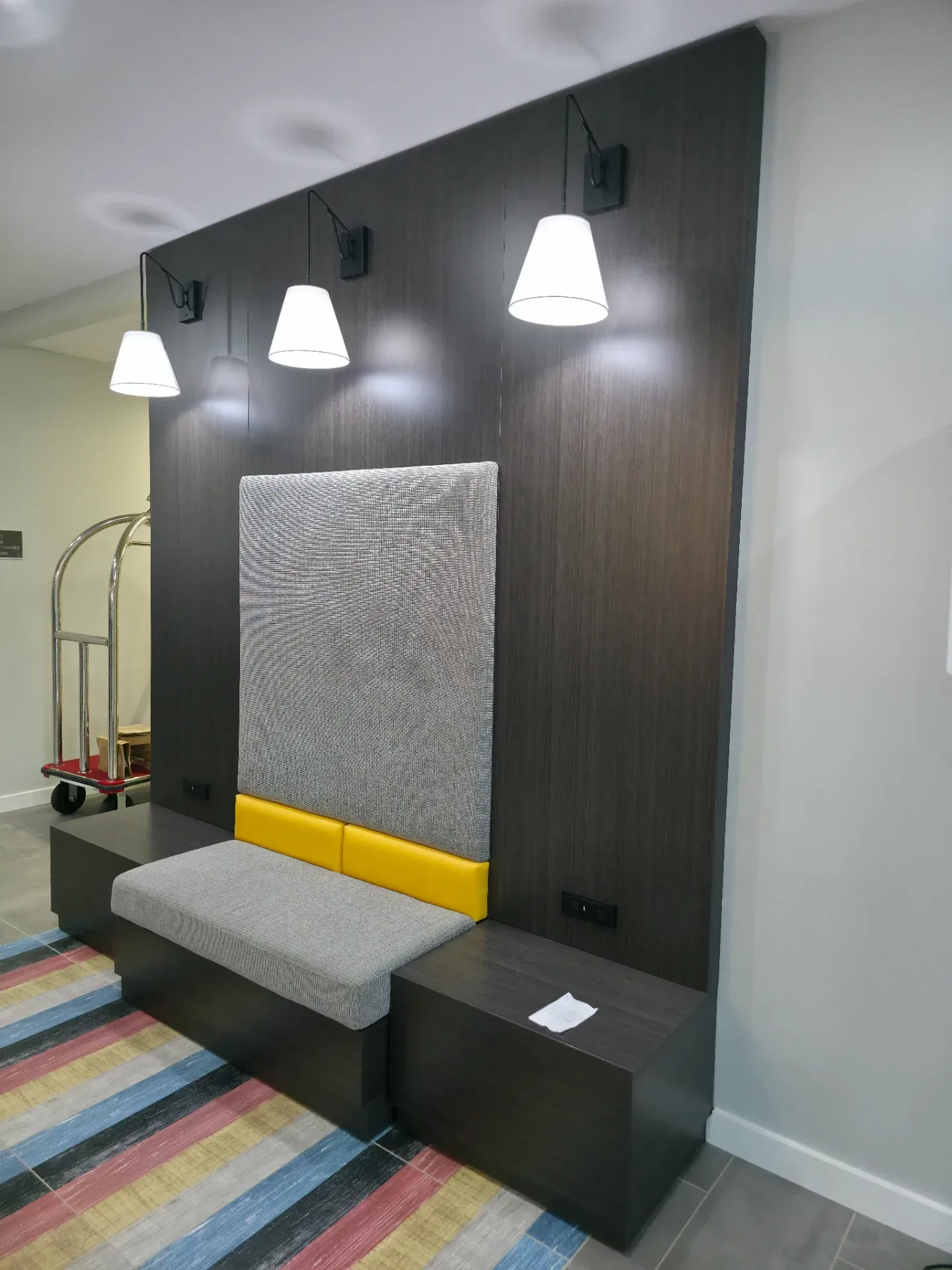 Dark panel lobby seating unit with upholstered back and seat cushions, flanked by pendant wall lights